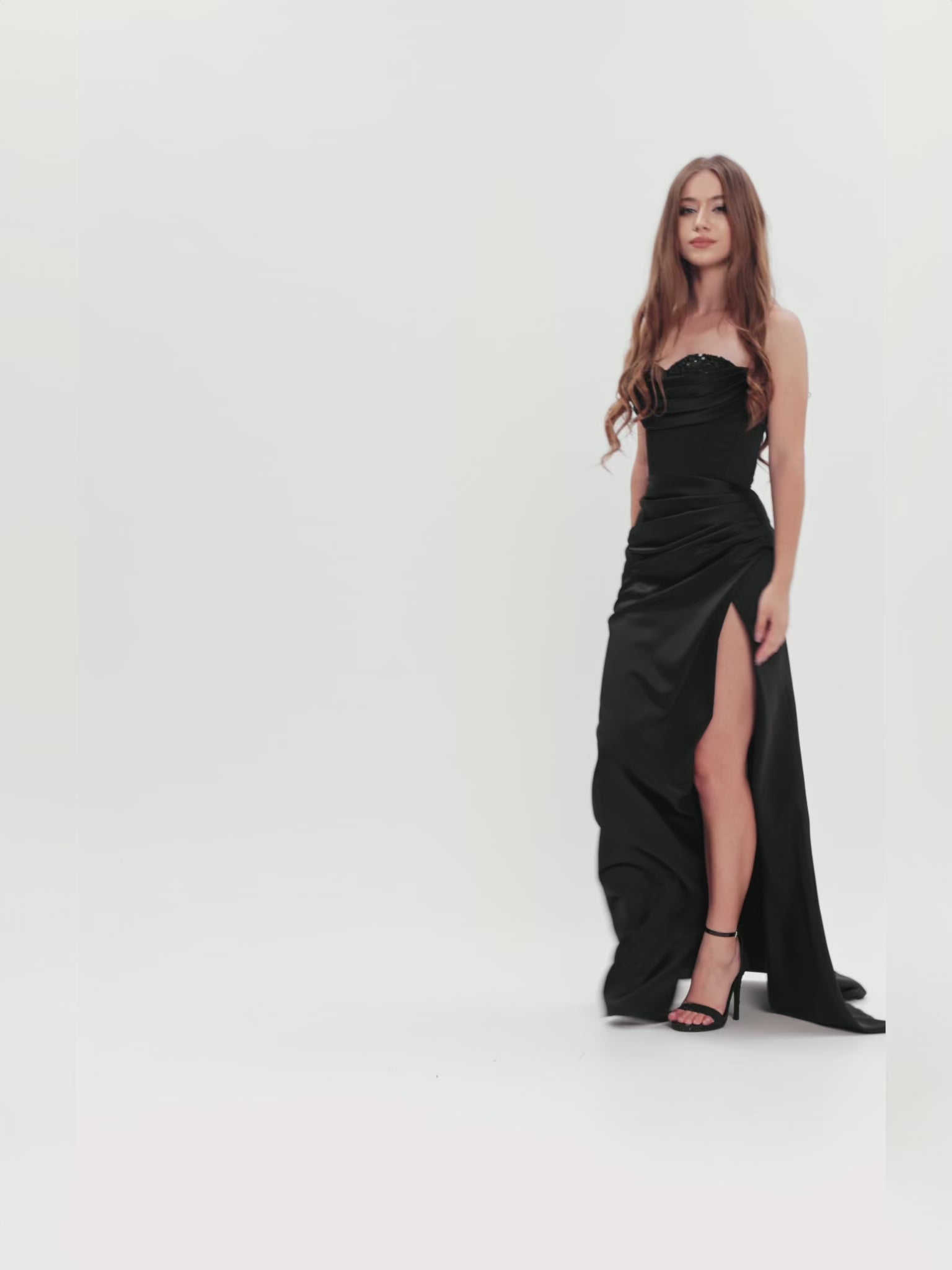 Model prezentând o rochie elegantă din satin negru cu corset și deschidere laterală, capturând fluiditatea materialului și silueta sofisticată.